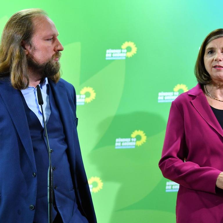 Katrin Göring-Eckardt und Anton Hofreiter stehen vor einer grünen Wand mit dem Logo der Partei.