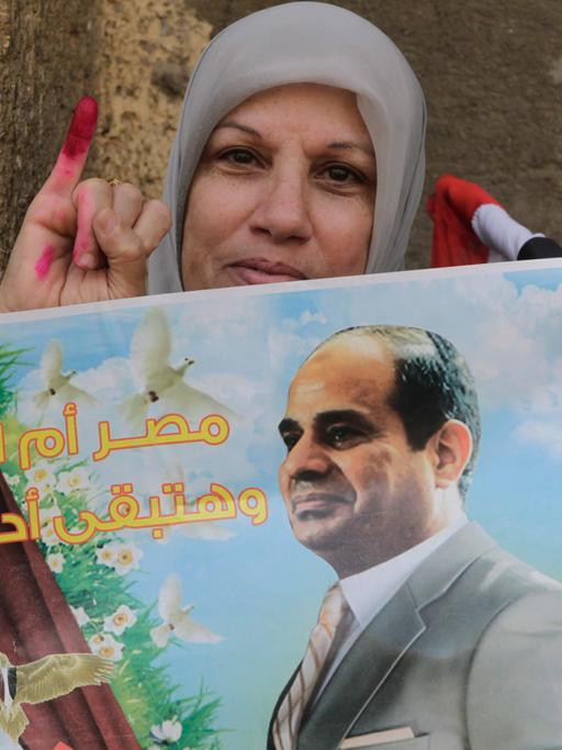 Eine Ägypterin nach der Wahl zeigt ihren mit Farbe markierten Finger, in der Hand ein Plakat mit Abdel Fattah al-Sissi.