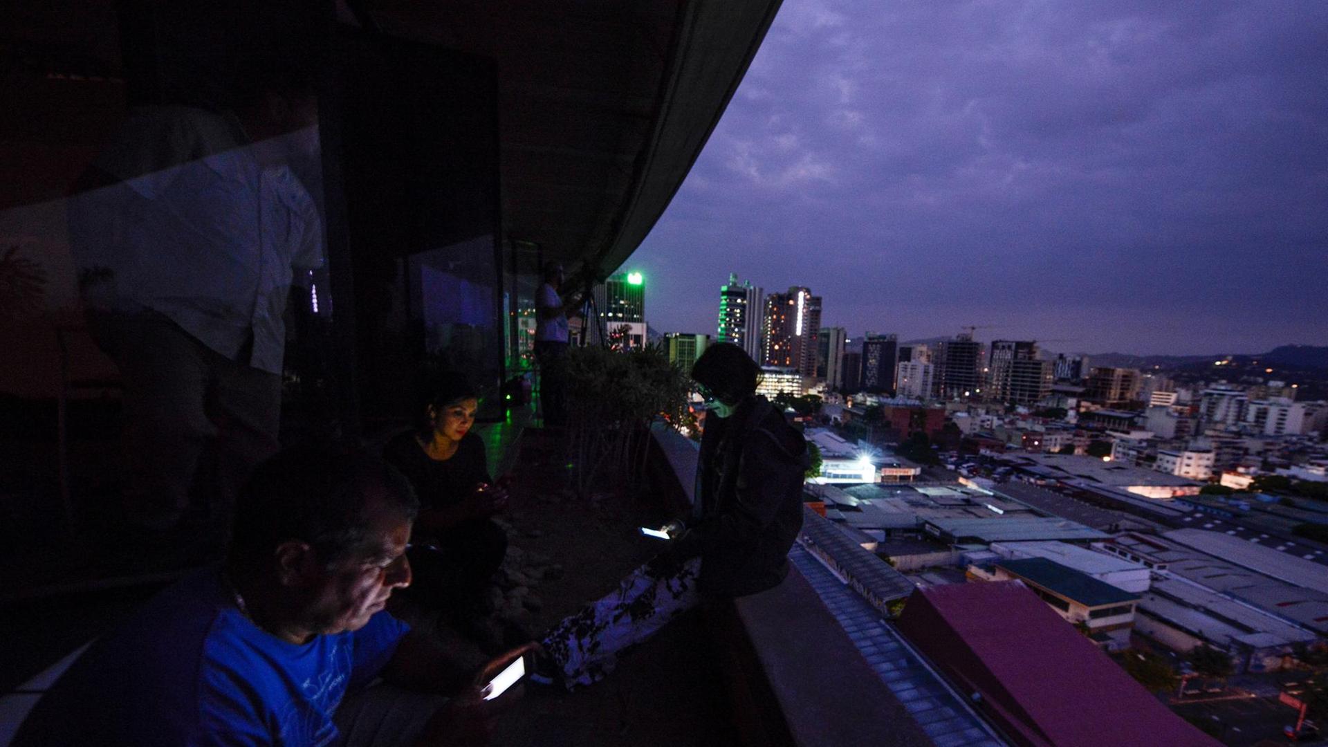 Journalisten blicken auf ihre Smartphones, während Venezuelas Hauptstadt Caracas im Dunkeln liegt