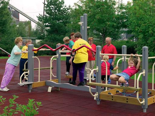 Während Kinder an einem Trainings- und Bewegungsgerät spielen, nutzen ältere Menschen dieses zur Fitness.