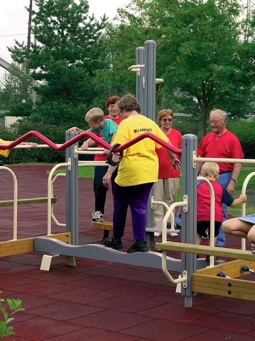 Während Kinder an einem Trainings- und Bewegungsgerät spielen, nutzen ältere Menschen dieses zur Fitness.