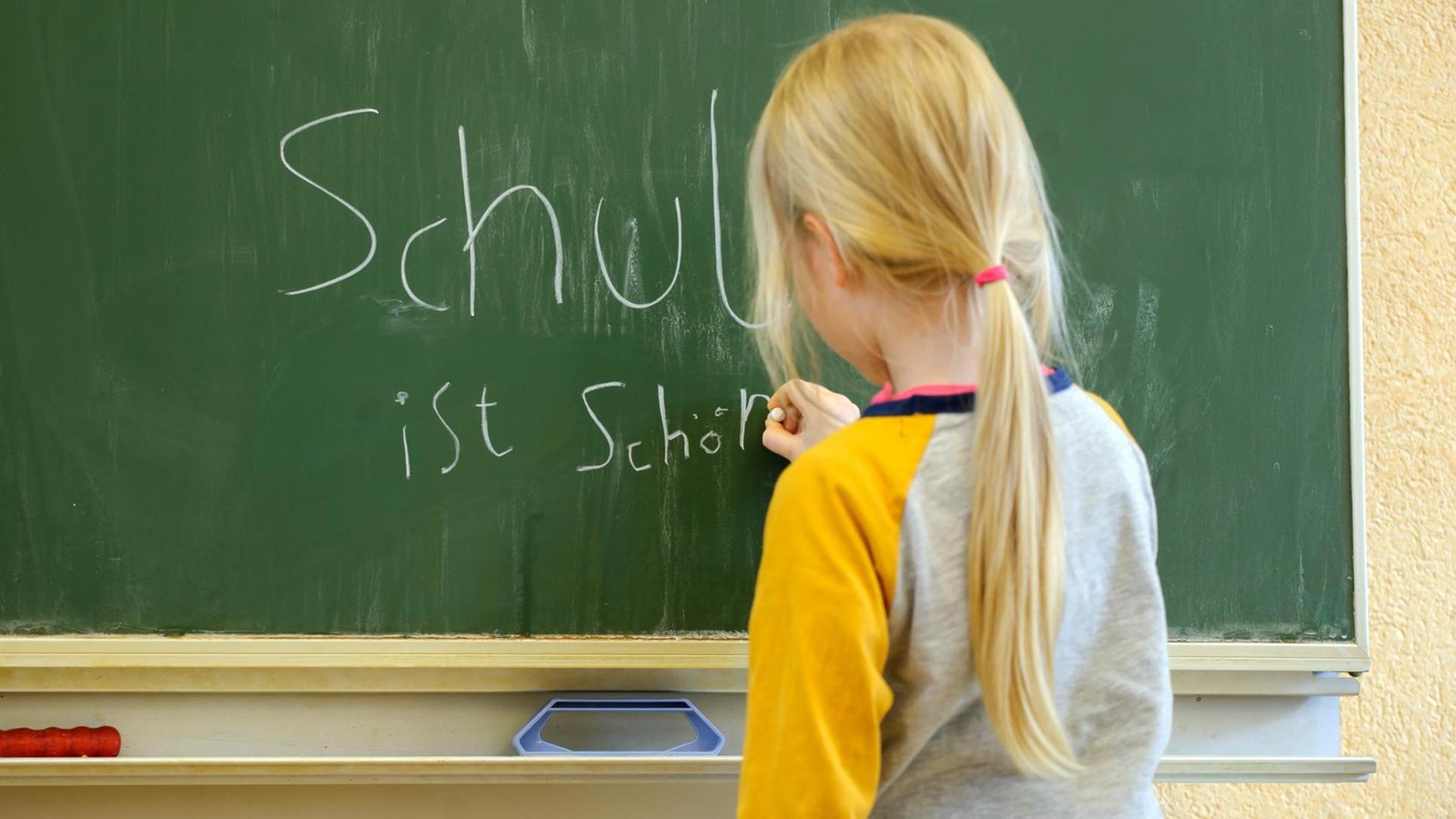 Ein Mädchen schreibt mit Kreide an eine Schultafel den Satz "Schule ist schön". Ein Mädchen schreibt mit Kreide an eine Schultafel den Satz "Schule ist schön".