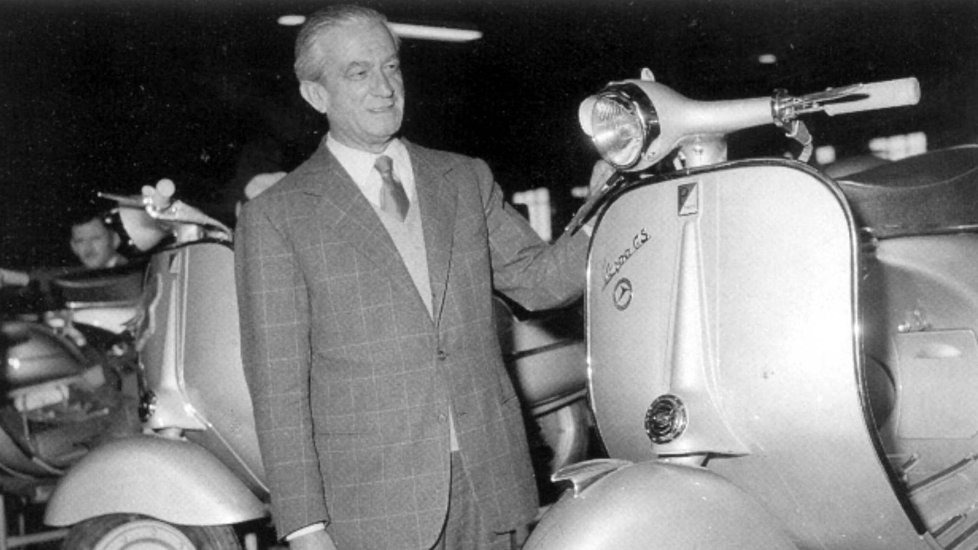 Ein Schwarzweiß-Foto zeigt einen älteren Mann mit kariertem Jacket. den Blick auf das Chassis einer Vespa gerichtet, die linke Hand auf den Lenker gelegt Ein Schwarzweiß-Foto zeigt einen älteren Mann mit kariertem Jacket. den Blick auf das Chassis einer Vespa gerichtet, die linke Hand auf den Lenker gelegt
