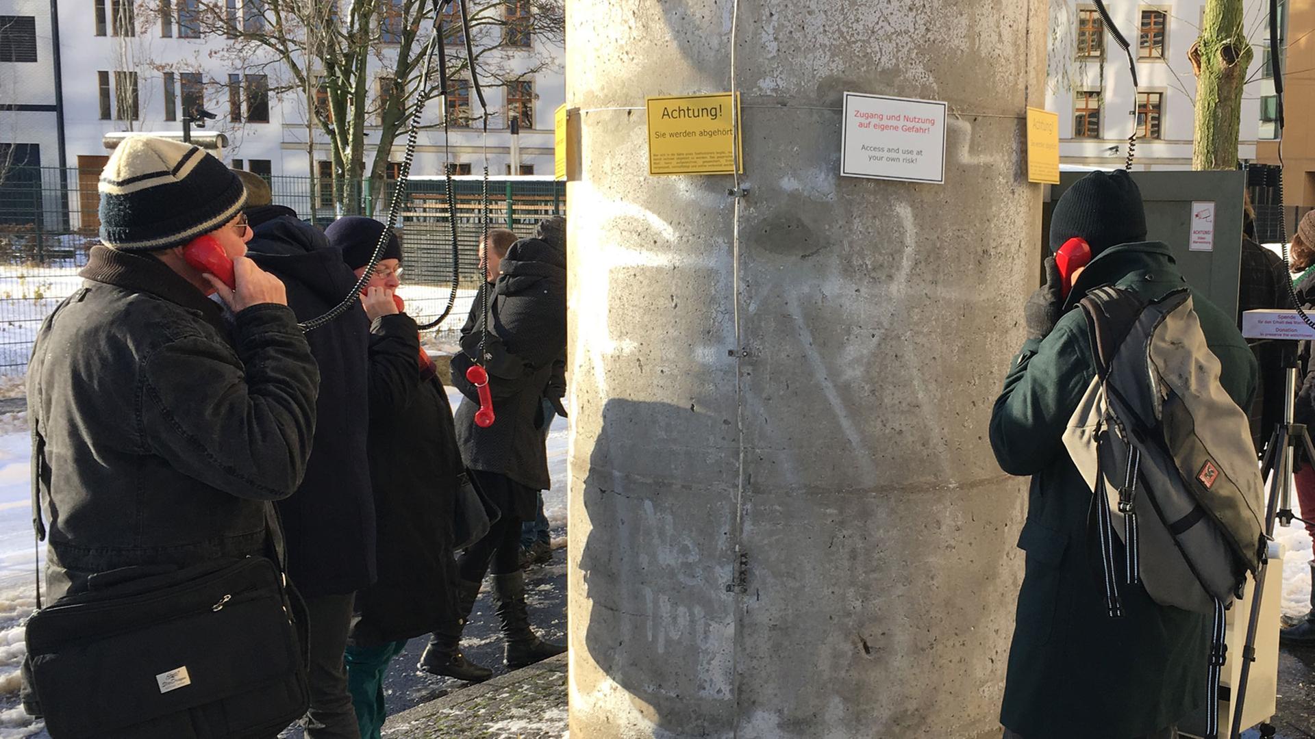 Besucher der temporären Kunstinstallation "Am Telefon sagt man nix" der Gruppe ÜB3R stehen im Januar 2016 um den Fuß eines ehemaligen DDR-Grenzwachturms in der Nähe des Potsdamer Platzes in Berlin-Mitte und halten Telefonhörer ans Ohr.