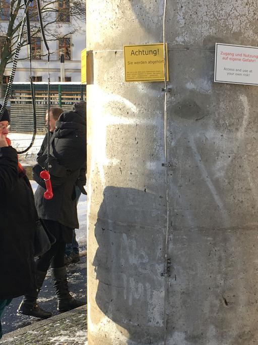 Besucher der temporären Kunstinstallation "Am Telefon sagt man nix" der Gruppe ÜB3R stehen im Januar 2016 um den Fuß eines ehemaligen DDR-Grenzwachturms in der Nähe des Potsdamer Platzes in Berlin-Mitte und halten Telefonhörer ans Ohr.