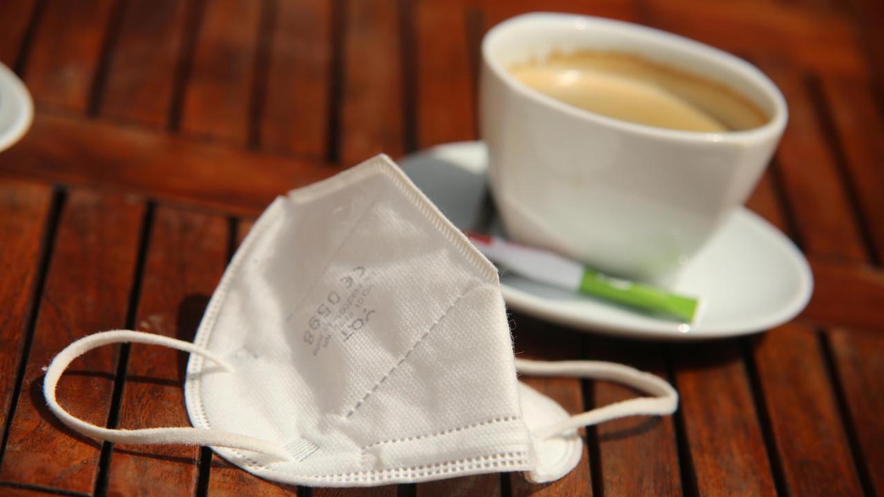 Neben einer Tasse Kaffee liegt eine FFP2-Maske auf dem Cafétisch Neben einer Tasse Kaffee liegt eine FFP2-Maske auf dem Cafétisch