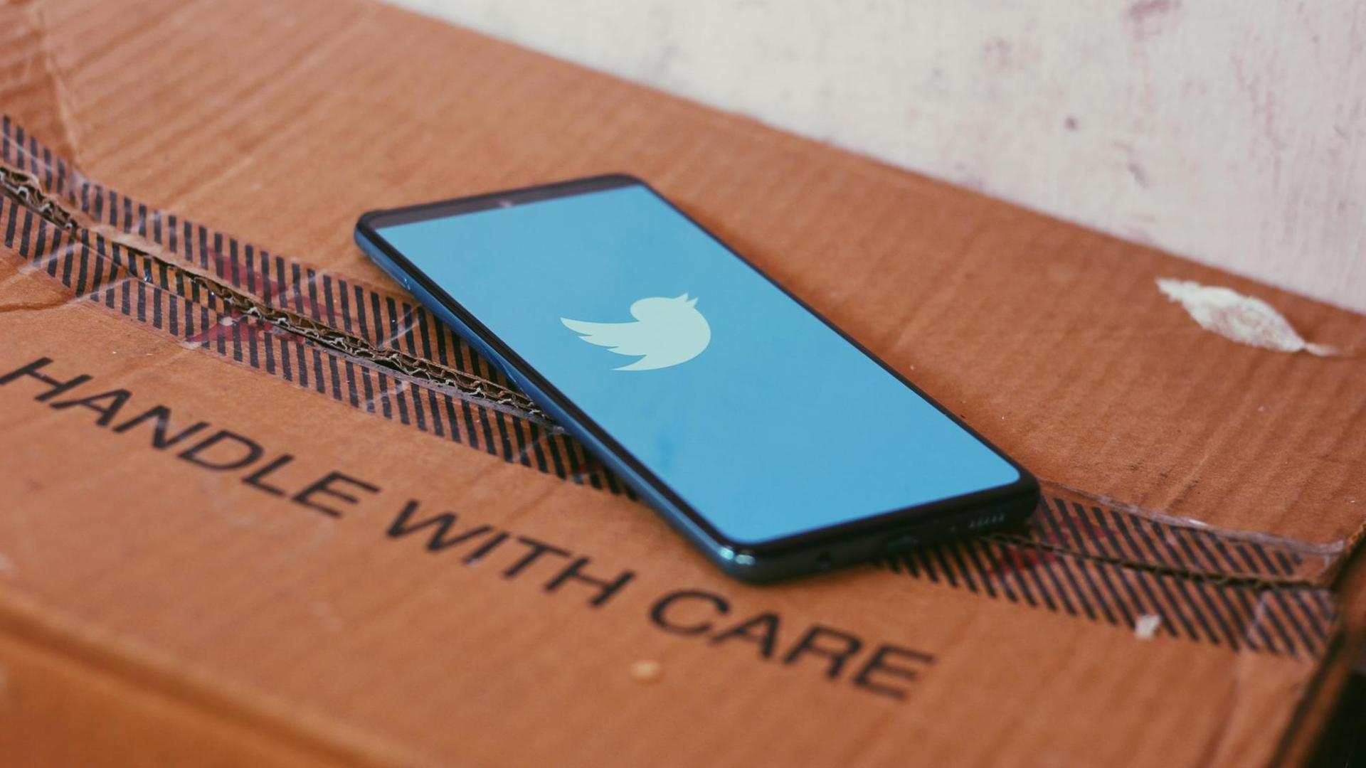 Ein Smartphone mit dem Twitterlogo liegt auf einem Paket mit der Aufschrift "HANDLE WITH CARE".