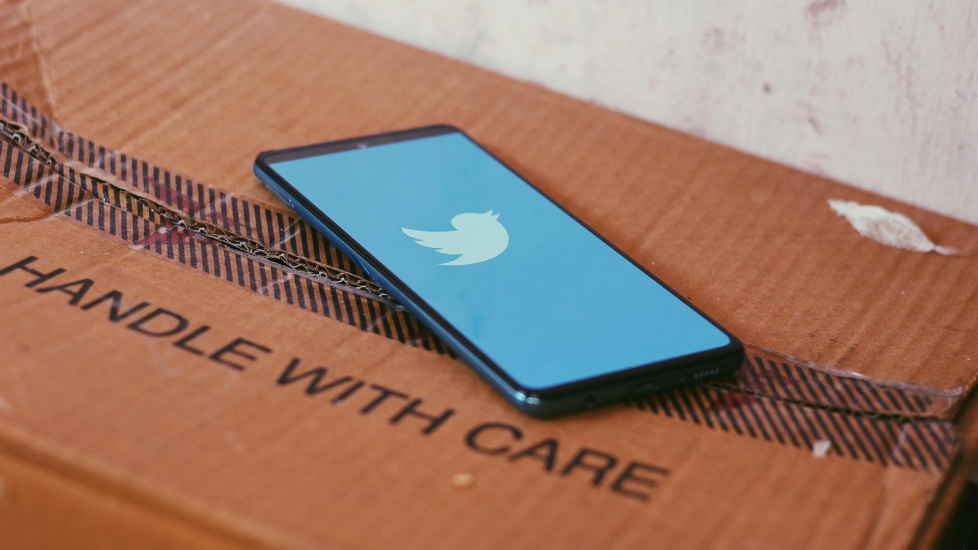 Ein Smartphone mit dem Twitterlogo liegt auf einem Paket mit der Aufschrift "HANDLE WITH CARE". Ein Smartphone mit dem Twitterlogo liegt auf einem Paket mit der Aufschrift "HANDLE WITH CARE".