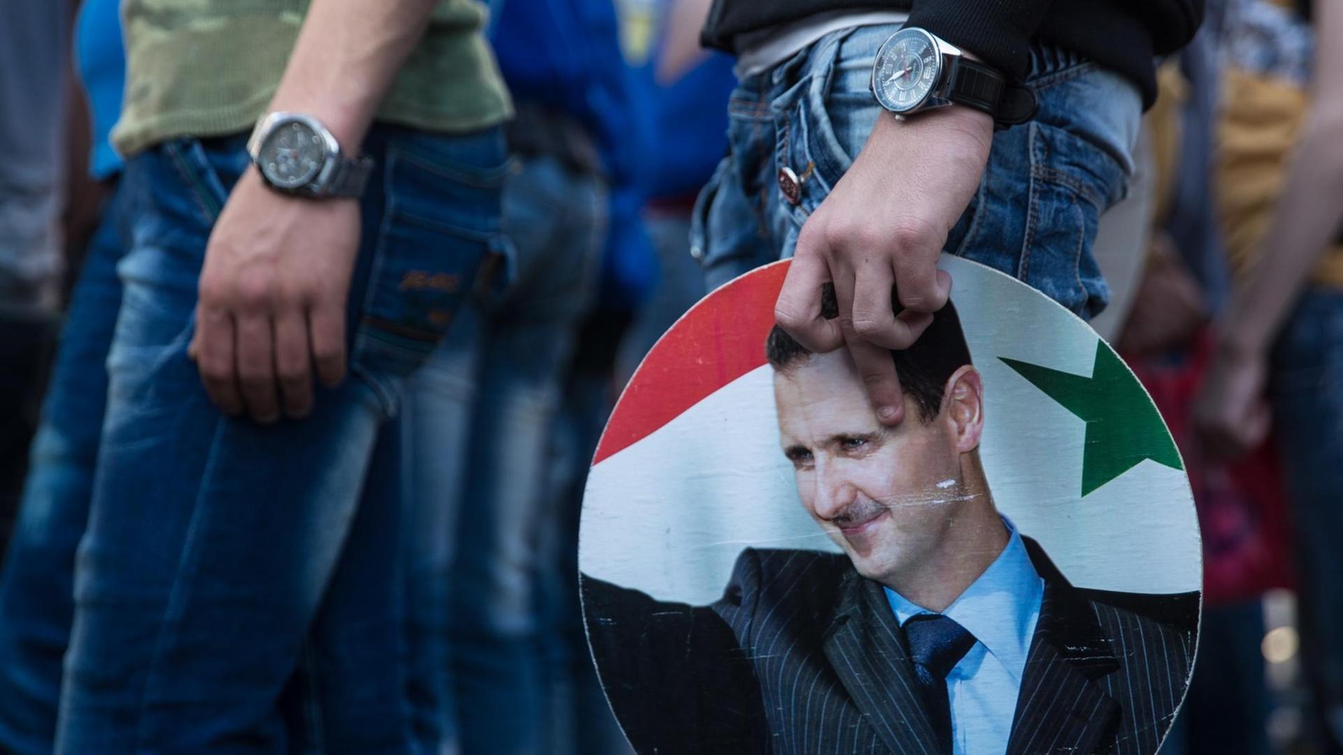 Demonstranten in Latakia bei einer Kundgebung für das Regime Assad, ein Schild mit seinem Konterfei in der Hand