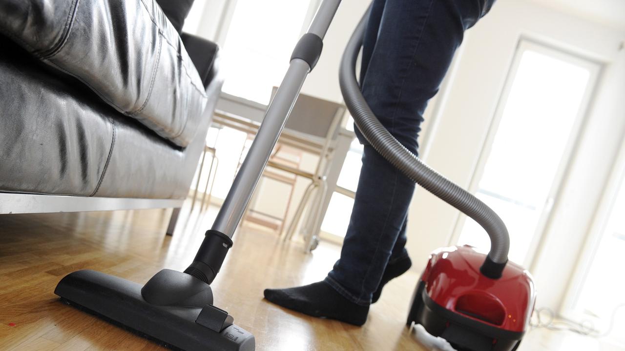 Eine Frau saugt mit einem Staubsauger den Fußboden eines Wohnzimmers. Eine Frau saugt mit einem Staubsauger den Fußboden eines Wohnzimmers.
