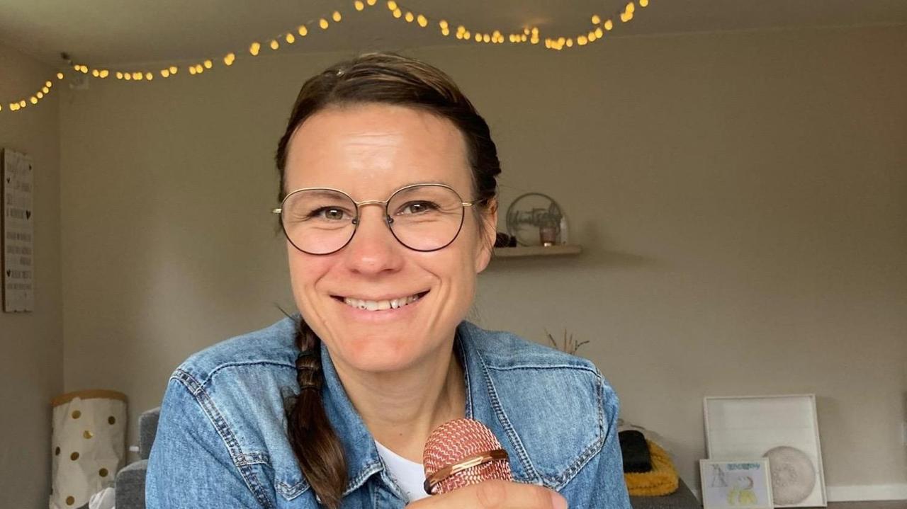 Daniela Lilienthal sitzt an einem Tisch und hält ein Mikrofon in der Hand. An der Zimmerdecke hängen Lichterketten. Daniela Lilienthal sitzt an einem Tisch und hält ein Mikrofon in der Hand. An der Zimmerdecke hängen Lichterketten.