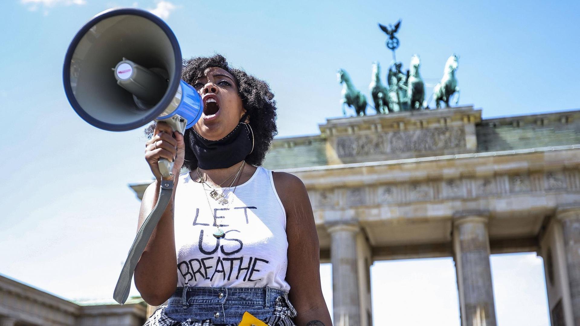 Eine Frau steht vor dem Brandenburger Tor, sie ruft in ein Megafon. Eine Frau steht vor dem Brandenburger Tor, sie ruft in ein Megafon.