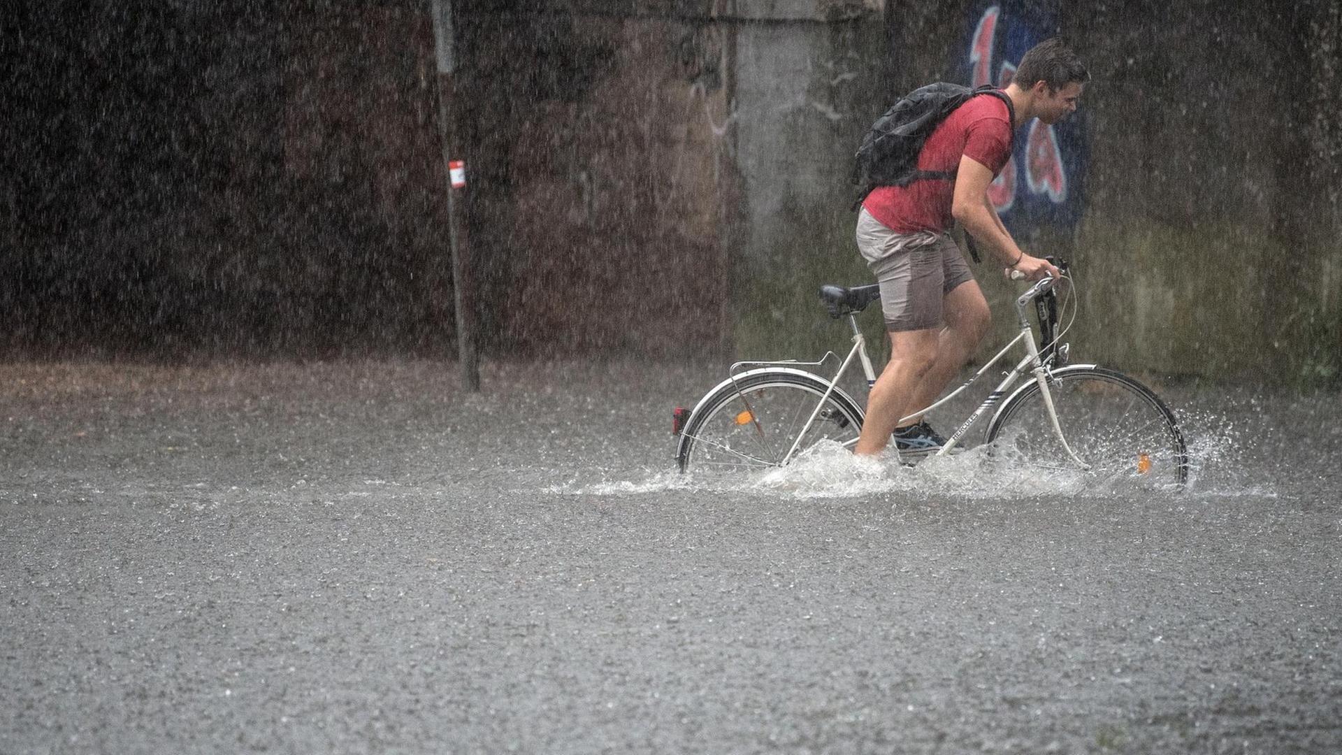 Ein Fahrradfahrer fährt auf einer überfluteten Straße in Köln im Wasser mit ihrem Rad.
