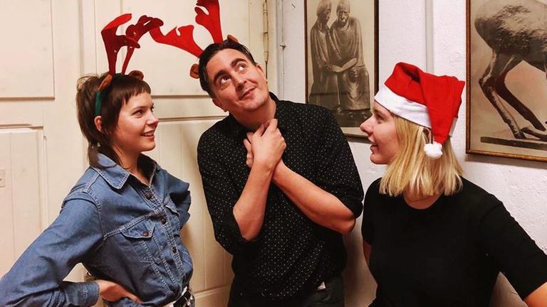 Zwei Frauen und ein Mann mit Weihnachtsmütz und Rehgeweih auf dem Kopf stehen vor einer hellen Wand. Zwei Frauen und ein Mann mit Weihnachtsmütz und Rehgeweih auf dem Kopf stehen vor einer hellen Wand.