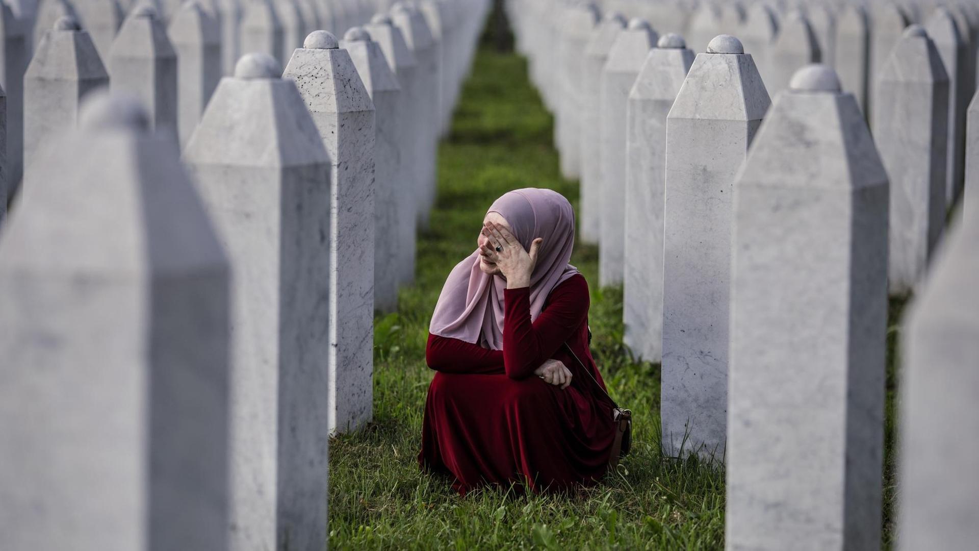 Eine bosnisch-muslimische Frau weint zwischen den Gräbern ihres Vaters, zweier Großväter und anderer enger Verwandter, auf dem Friedhof in Potocari in der Nähe von Srebrenica, Bosnien und Herzegowina. Eine bosnisch-muslimische Frau weint zwischen den Gräbern ihres Vaters, zweier Großväter und anderer enger Verwandter, auf dem Friedhof in Potocari in der Nähe von Srebrenica, Bosnien und Herzegowina.