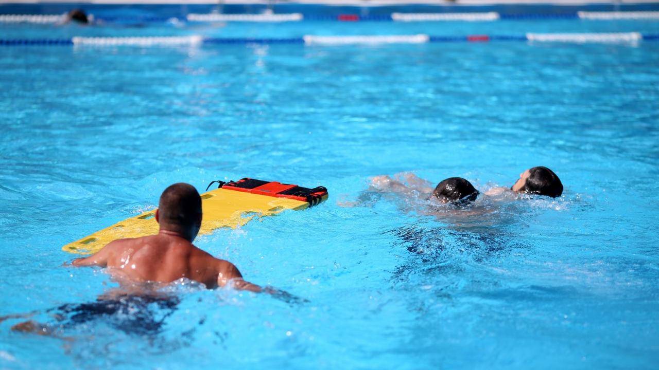 Drei Rettungsschwimmer simulieren die Bergung einer bewusstlosen Person mit Hilfe eines neuen Spineboards am 18.07.2016 im Freibad Saline in Halle/Saale (Sachsen-Anhalt) vor. Das Freibad in Halle wurde von der DRK Wasserwacht Halle einem Sicherheitscheck unterzogen und erhielt das Siegel «Sicheres Schwimmbad». Moderne Rettungsmittel, und ausgebildete Rettungsschwimmer sowie Ersthelfer sind Voraussetzungen dafür. Drei Rettungsschwimmer simulieren die Bergung einer bewusstlosen Person mit Hilfe eines neuen Spineboards am 18.07.2016 im Freibad Saline in Halle/Saale (Sachsen-Anhalt) vor. Das Freibad in Halle wurde von der DRK Wasserwacht Halle einem Sicherheitscheck unterzogen und erhielt das Siegel «Sicheres Schwimmbad». Moderne Rettungsmittel, und ausgebildete Rettungsschwimmer sowie Ersthelfer sind Voraussetzungen dafür.