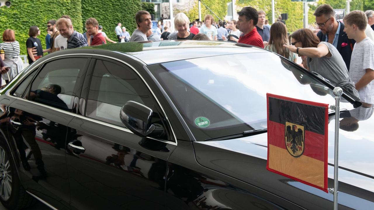 An dem schwarzen Wagen ist eine Deutschland-Fahne mit Adler angebracht. Hinter dem Auto stehen zahlreiche Besucher, die es betrachten. Im Hintergrund das Kanzleramt.