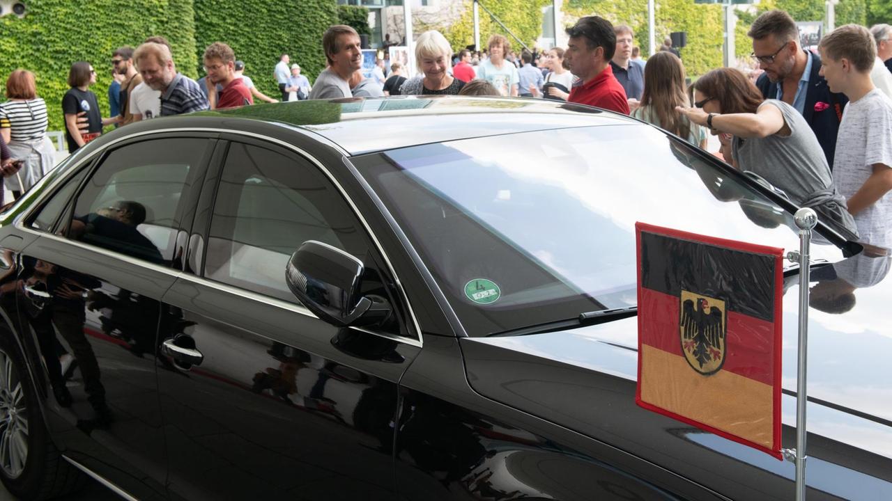 An dem schwarzen Wagen ist eine Deutschland-Fahne mit Adler angebracht. Hinter dem Auto stehen zahlreiche Besucher, die es betrachten. Im Hintergrund das Kanzleramt. An dem schwarzen Wagen ist eine Deutschland-Fahne mit Adler angebracht. Hinter dem Auto stehen zahlreiche Besucher, die es betrachten. Im Hintergrund das Kanzleramt.