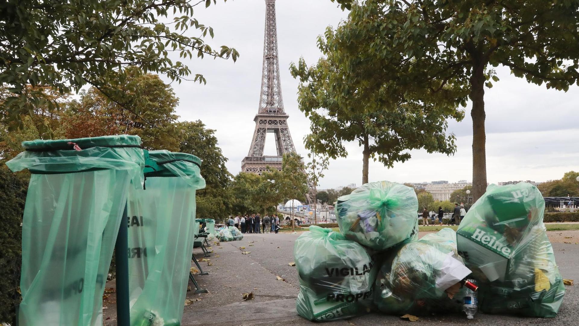 Plastiktüten mit Müll liegen neben Mülltonnen in einer Pariser Straße mit dem Eiffelturm im Hintergrund.