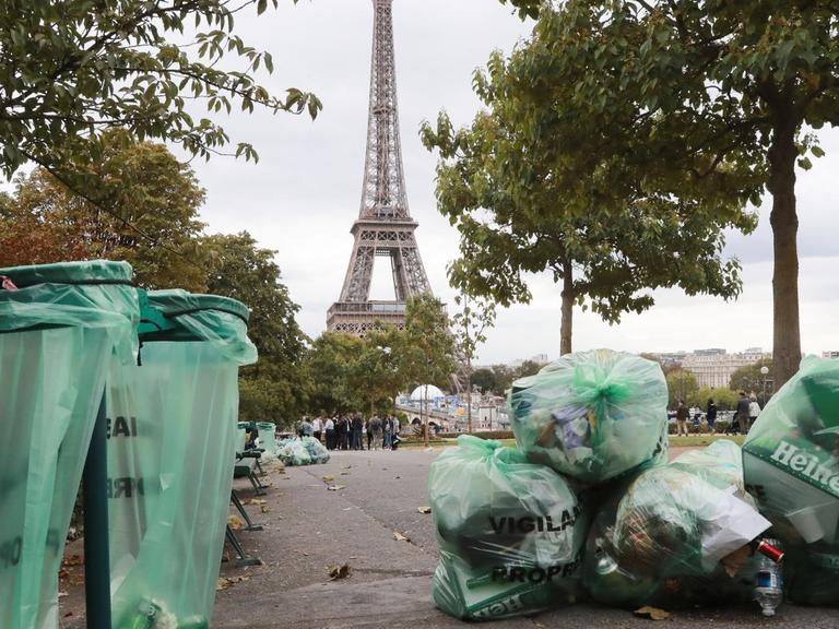 Plastiktüten mit Müll liegen neben Mülltonnen in einer Pariser Straße mit dem Eiffelturm im Hintergrund.