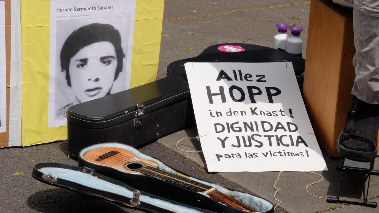 Neben einem Ukulelenkoffer liegt ein handbemaltes Schild mit der Aufschrift: "Allez Hopp in den Knast" Neben einem Ukulelenkoffer liegt ein handbemaltes Schild mit der Aufschrift: "Allez Hopp in den Knast"