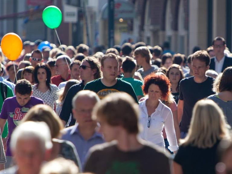 Eine Fußgängerzone mit vielen Menschen bei Sonnenschein.