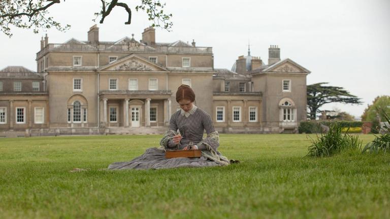 Eine Frau sitzt auf einer großen Rasenfläche vor einem großen Landhaus in England