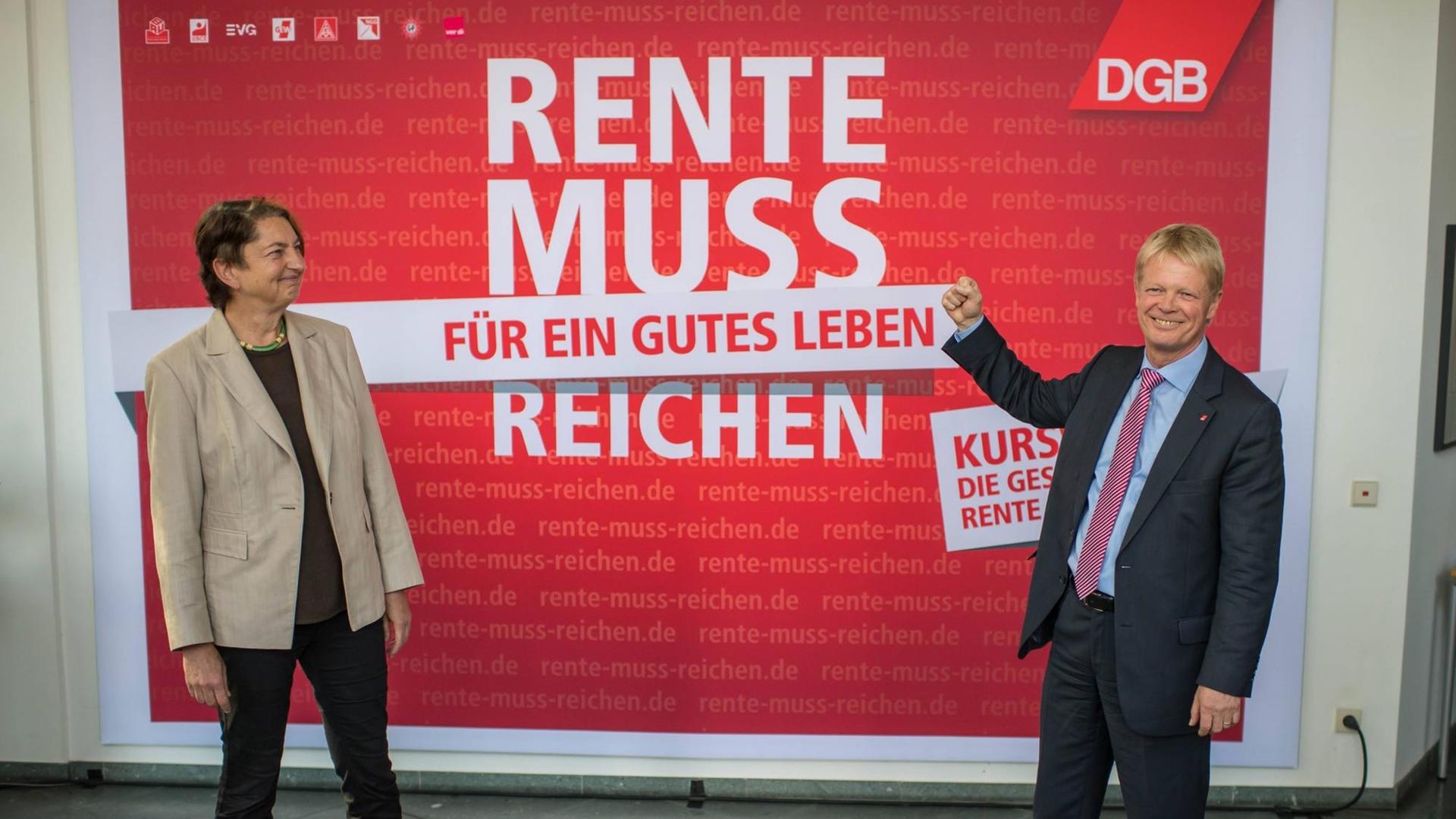 Buntenbach und Hoffmann stehen lachend vor einem rot-weißen Plakat mit der Aufschrift "Rente muss für ein gutes Leben reichen"
