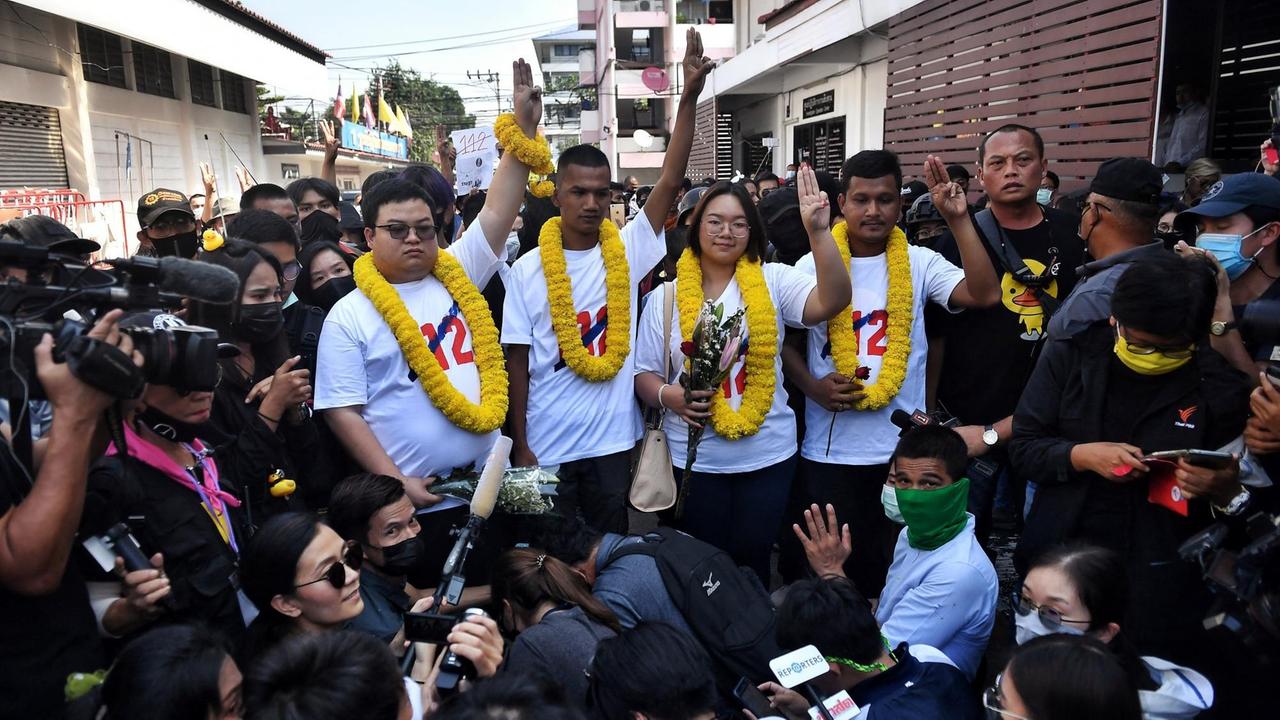 Parit "Penguin" Chiwarak, Panupong "Mike" Jadnok, Panusaya "Rung" Sithijirawattanakul und Shinawat Chankrachang posieren von Pressevertretern umringt für ein Gruppenfoto mit dem Drei-Finger-Gruß. Parit "Penguin" Chiwarak, Panupong "Mike" Jadnok, Panusaya "Rung" Sithijirawattanakul und Shinawat Chankrachang posieren von Pressevertretern umringt für ein Gruppenfoto mit dem Drei-Finger-Gruß.