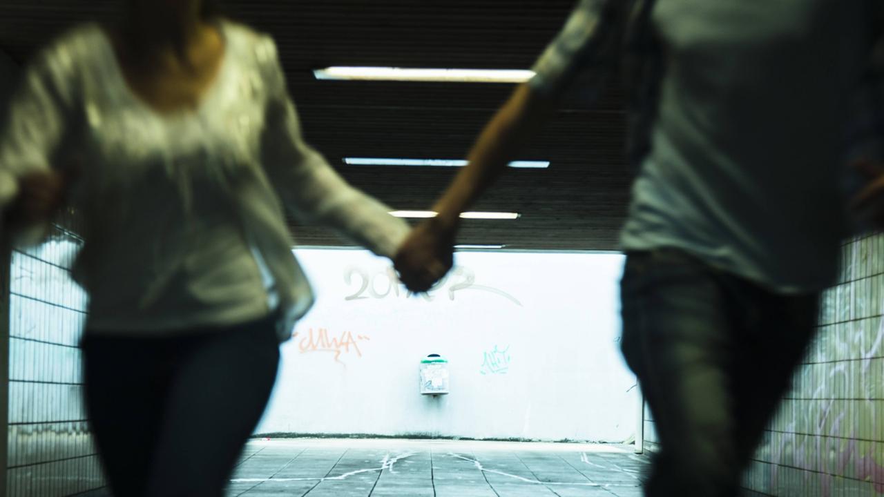Zwei Jugendliche laufen Hand in Hand durch eine Unterführung