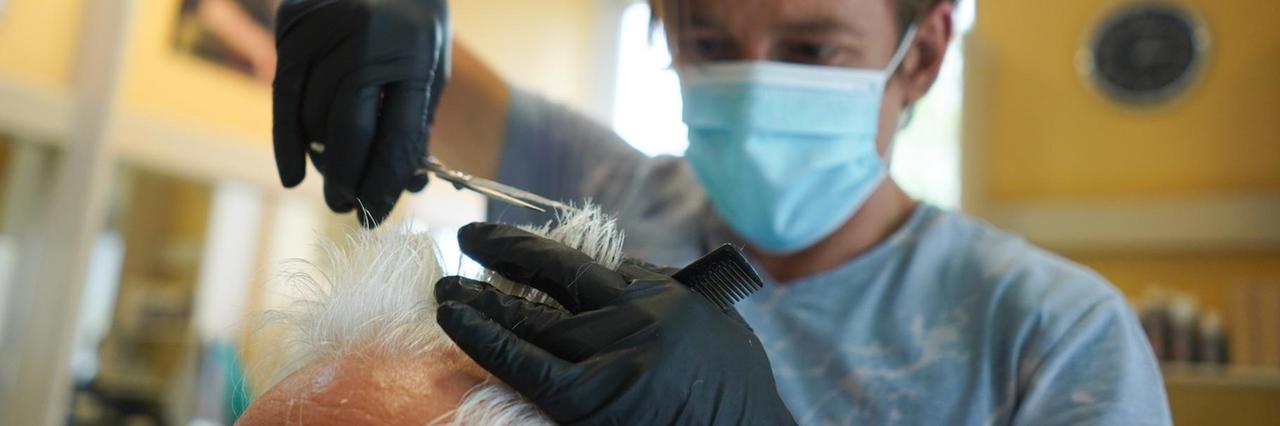 Ein Friseur mit Mundschutz schneidet einem Kunden die Haare. Ein Friseur mit Mundschutz schneidet einem Kunden die Haare.