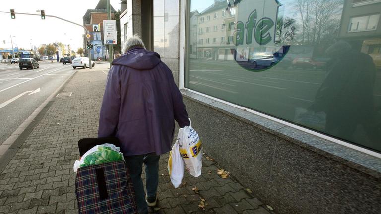 Eine ältere Dame verlässt bepackt mit Tragetaschen und einem gefüllten Trolley die "Kasseler Tafel", in der sie zuvor Lebensmittel bezogen hat.