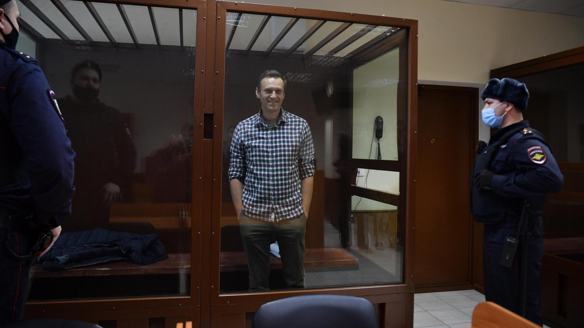 Alexej Nawalny steht in einem Gerichtssaal in einem Glaskasten und lächelt. Alexej Nawalny steht in einem Gerichtssaal in einem Glaskasten und lächelt.