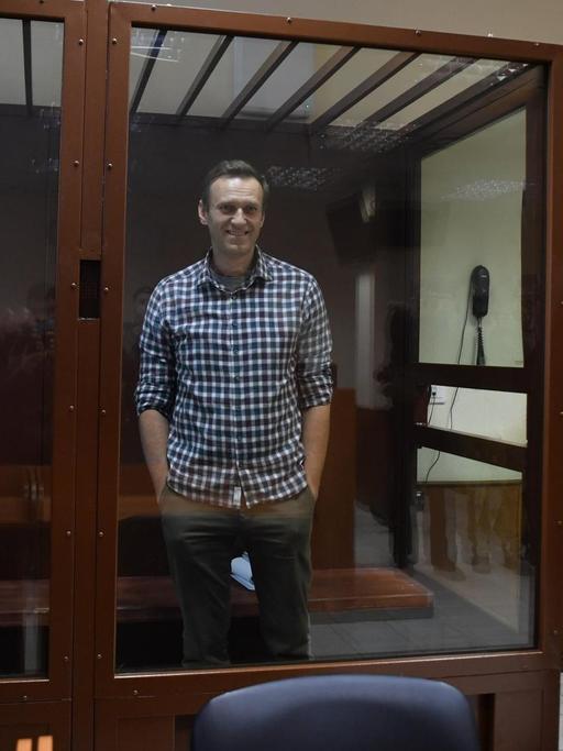 Alexej Nawalny steht in einem Gerichtssaal in einem Glaskasten und lächelt.