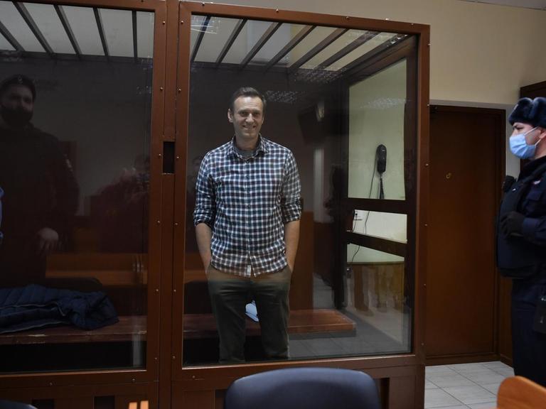 Alexej Nawalny steht in einem Gerichtssaal in einem Glaskasten und lächelt.