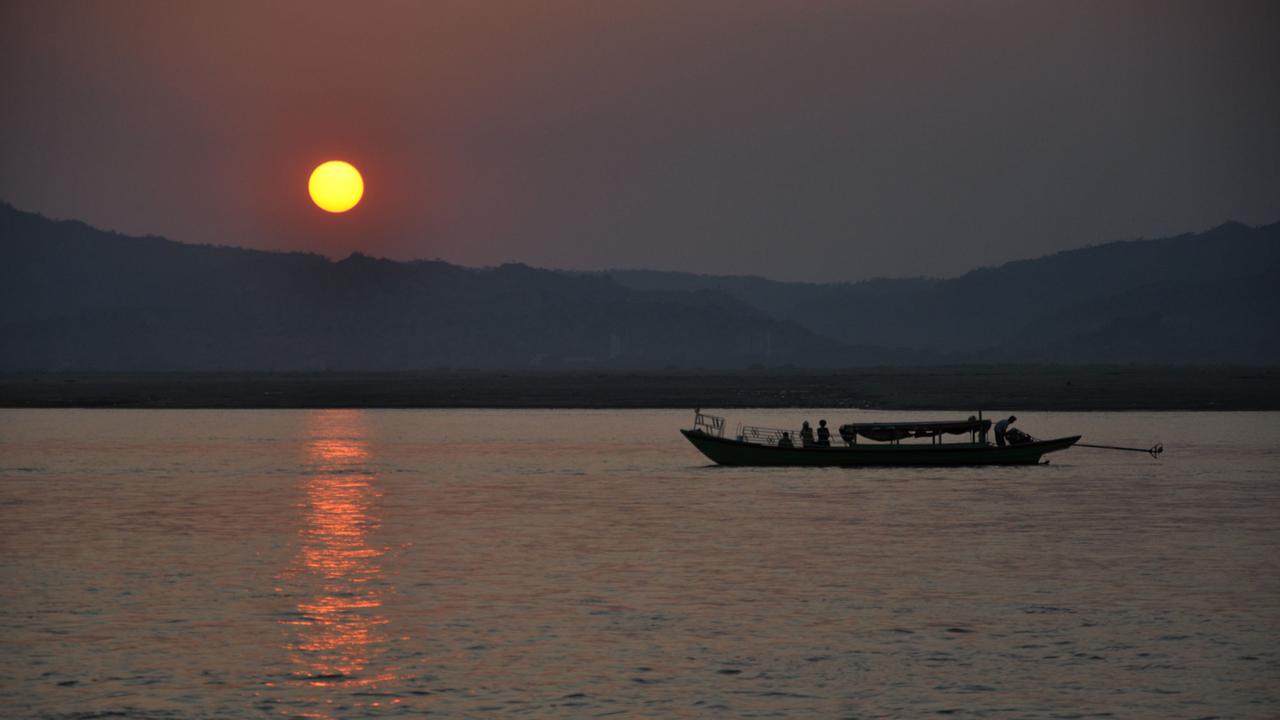 Die Sonne geht über dem burmesischen Fluss Irrawaddy in Myanmar. Ein Boot fährt auf dem Wasser. Die Sonne geht über dem burmesischen Fluss Irrawaddy in Myanmar. Ein Boot fährt auf dem Wasser.