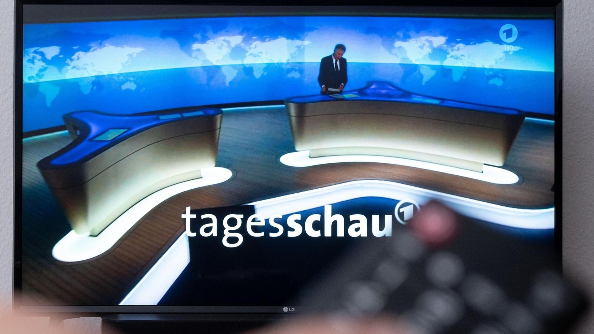 Ein Mann hält eine Fernbedienung vor einen Fernseher, auf dem die Tagesschau läuft. Ein Mann hält eine Fernbedienung vor einen Fernseher, auf dem die Tagesschau läuft.