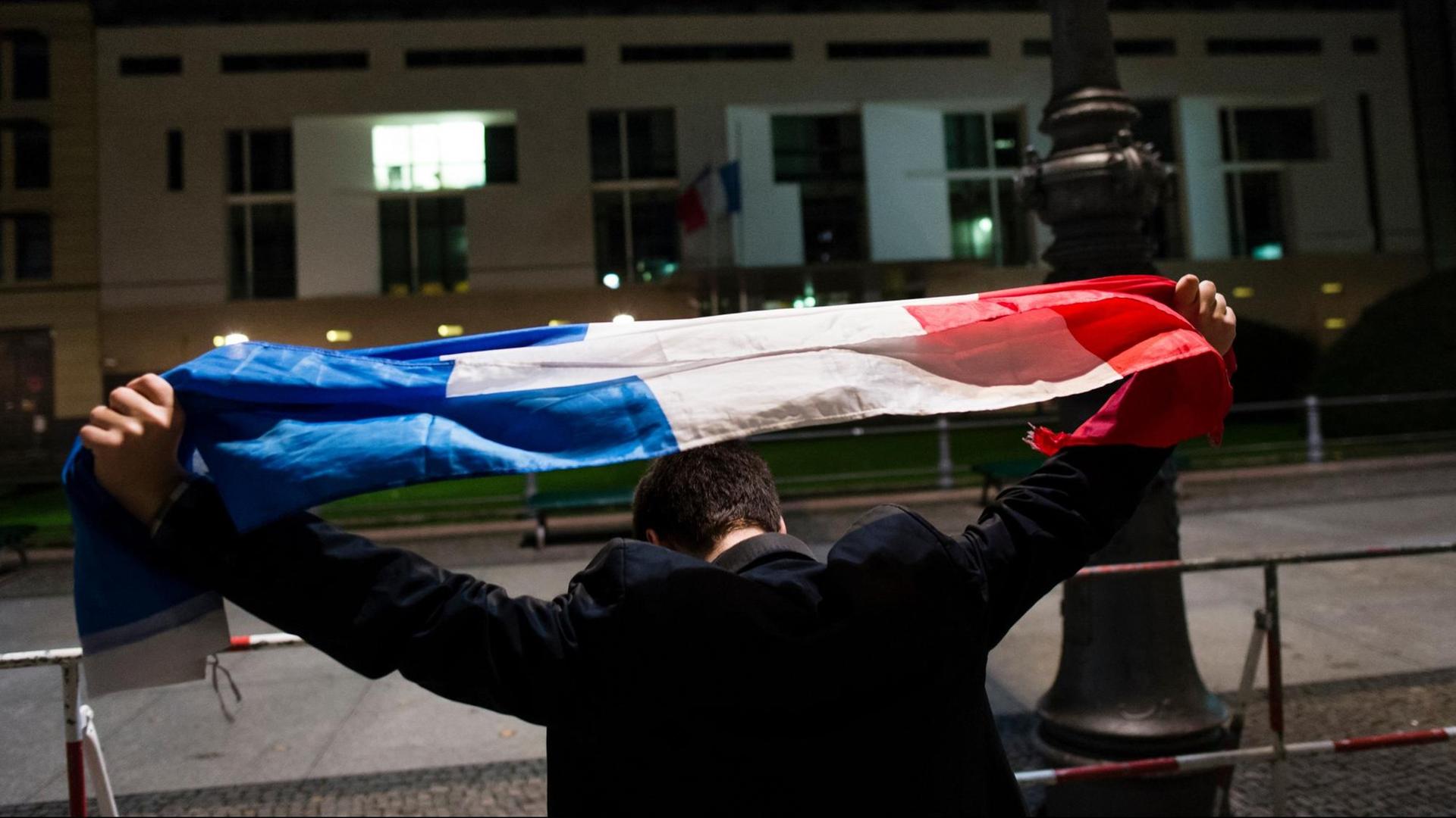 Ein Mann hält am 14.11.2015 vor der Französischen Botschaft in Berlin, die Flagge Frankreichs über seinen Kopf. Bei den Angriffen . Ein Mann hält am 14.11.2015 vor der Französischen Botschaft in Berlin, die Flagge Frankreichs über seinen Kopf. Bei den Angriffen .