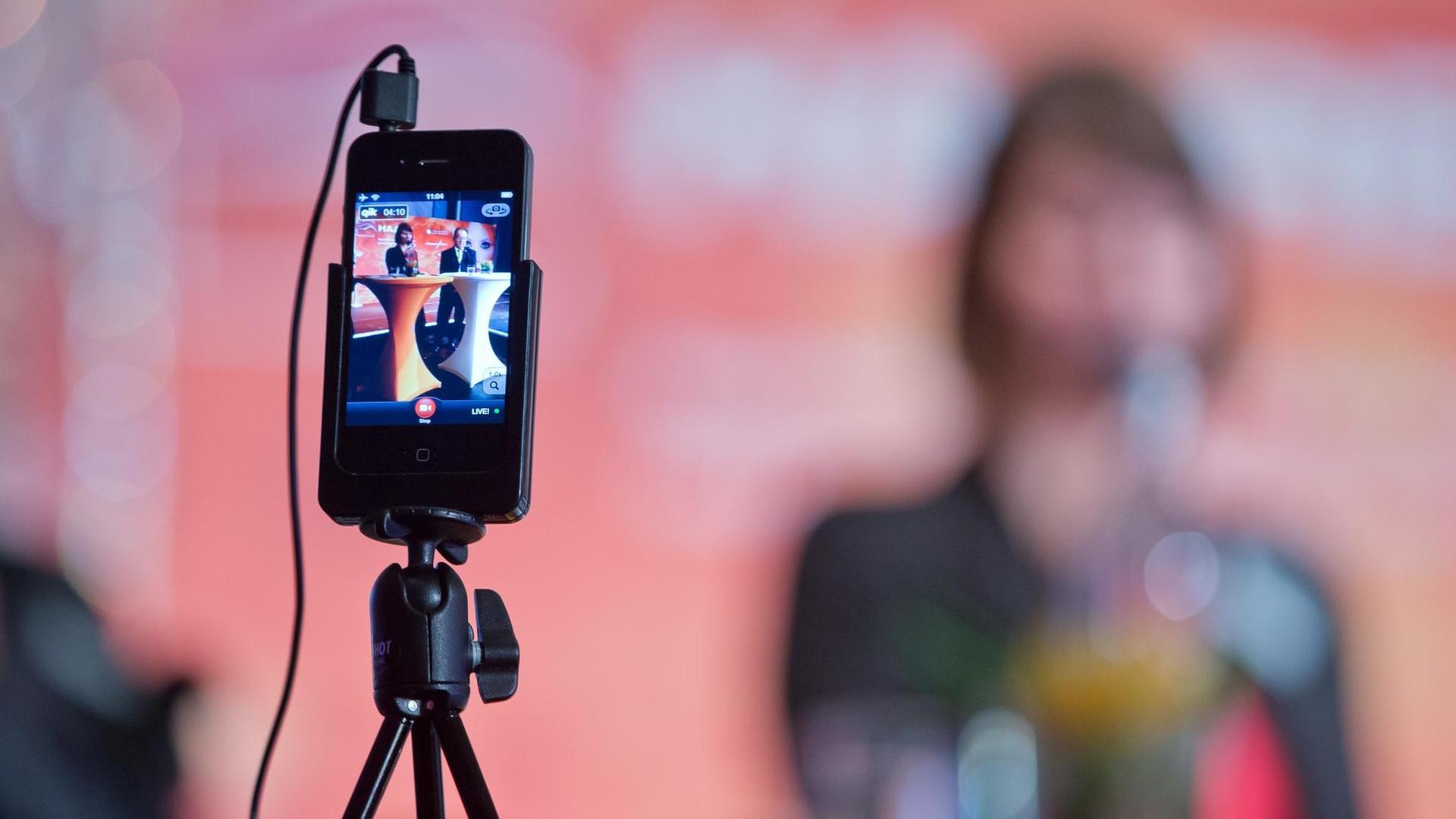 Ein Smartphone ist während einer Pressekonferenz auf einem Stativ angebracht, um diese zu filmen. Ein Smartphone ist während einer Pressekonferenz auf einem Stativ angebracht, um diese zu filmen.
