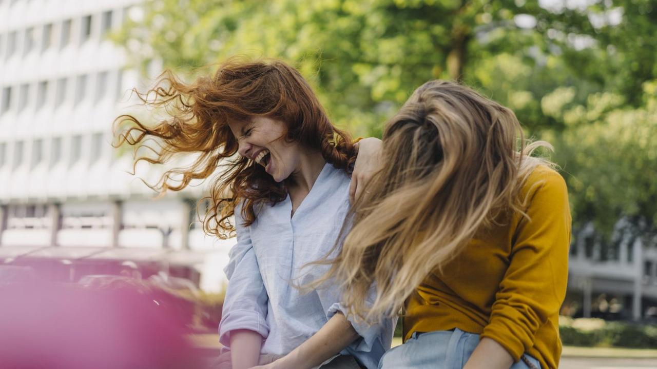 Zwei Frauen sitzen nebeneinander und schütten sich aus vor Lachen. Zwei Frauen sitzen nebeneinander und schütten sich aus vor Lachen.