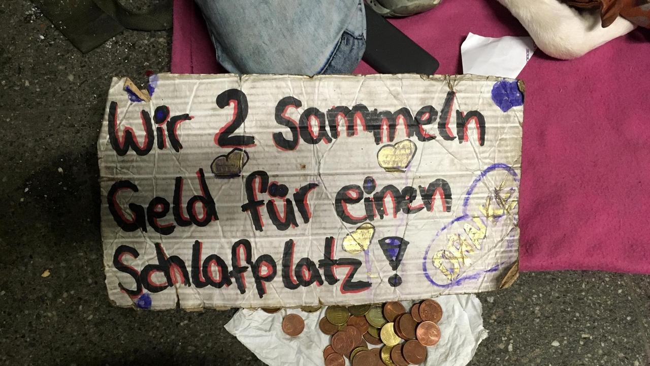 Ein Sammelbecher mit etwas Kleingeld, dazu ein Schild: "Wir zwei sammeln für einen Schlafplatz" Ein Sammelbecher mit etwas Kleingeld, dazu ein Schild: "Wir zwei sammeln für einen Schlafplatz"