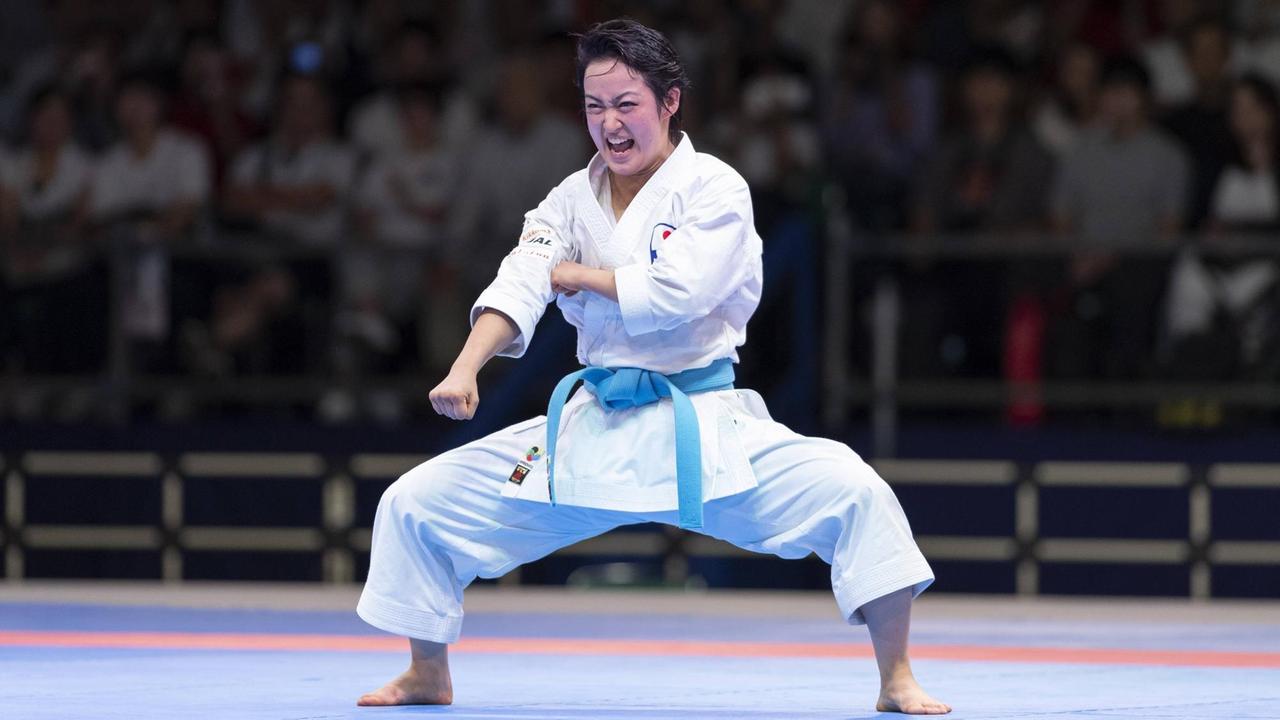 Kiyou Shimizu im Karateanzug mit blauem Gürtel steht breitbeinig in einer Arena, streckt die rechte Faust vor und schreit. Im Hintergrund sind Zuschauer zu sehen. Kiyou Shimizu im Karateanzug mit blauem Gürtel steht breitbeinig in einer Arena, streckt die rechte Faust vor und schreit. Im Hintergrund sind Zuschauer zu sehen.