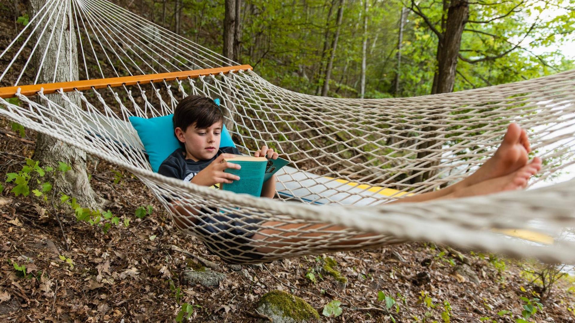 Young boy laying in a woven hammock relaxing and reading a book. Buck Lake, ON, Canada PUBLICATIONxINxGERxSUIxAUTxONLY CR_DOHO200904J-485083-01 ,model released, Symbolfoto Young boy laying in a woven hammock relaxing and reading a book. Buck Lake, ON, Canada PUBLICATIONxINxGERxSUIxAUTxONLY CR_DOHO200904J-485083-01 ,model released, Symbolfoto