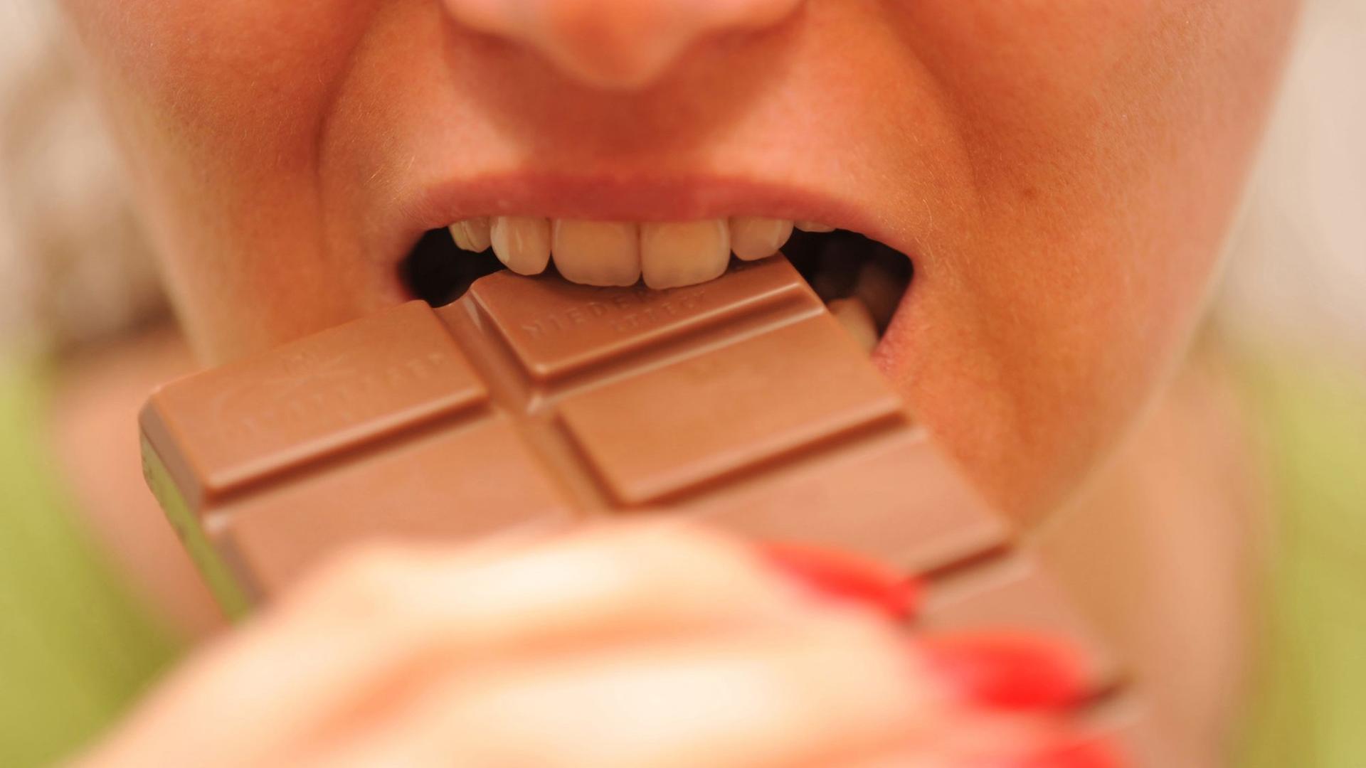 EIne Frau beißt in eine Tafel Schokolade