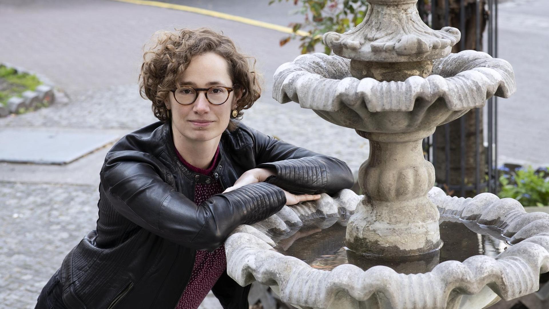 Elsa Koester steht an einen Brunnen gelehnt und schaut in die Kamera Elsa Koester steht an einen Brunnen gelehnt und schaut in die Kamera