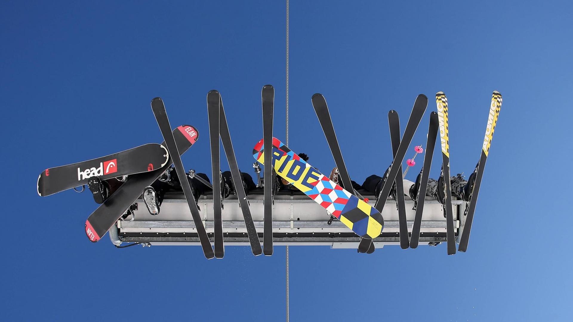 Ein Skilift im Sauerland, von unten aufgenommen. Zu sehen sind Skier und Snowboards vor blauem Himmel.