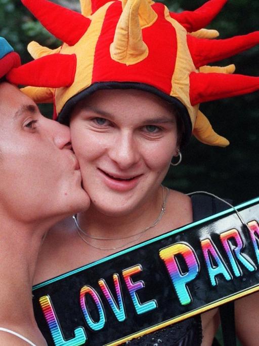 Mit einem Schild "Love Parade 97" in der Hand demonstriert ein Pärchen, mit Hüten bunt geschmückt, den Sinn des Festes - und gibt sich einen Kuss. Fast eine Million Techno-Fans haben am 12.07.1997 bei der Love Parade in Berlin die weltweit größte Party des Jahres gefeiert.