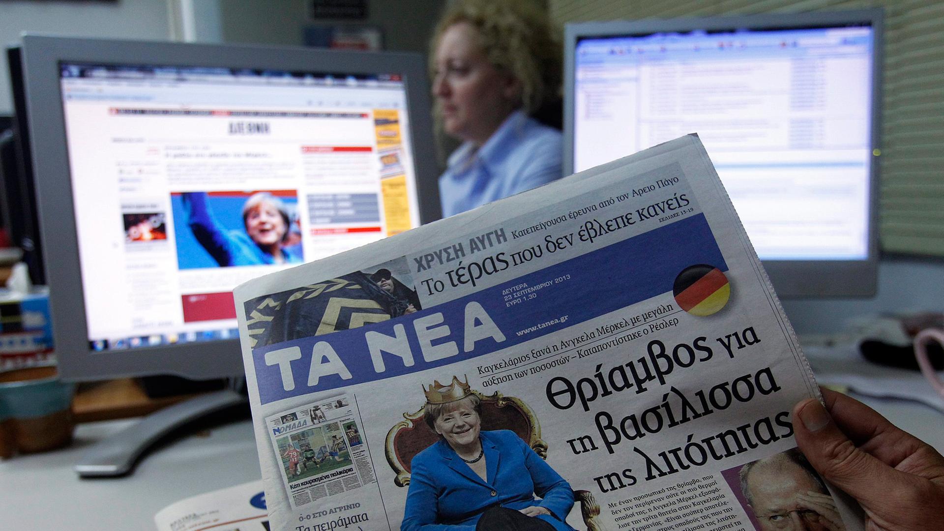 Ein griechischer Journalist hält eine Tageszeitung in der Hand, auf der Bundeskanzlerin Merkel auf einem Thron sitzt. Ein griechischer Journalist hält eine Tageszeitung in der Hand, auf der Bundeskanzlerin Merkel auf einem Thron sitzt.
