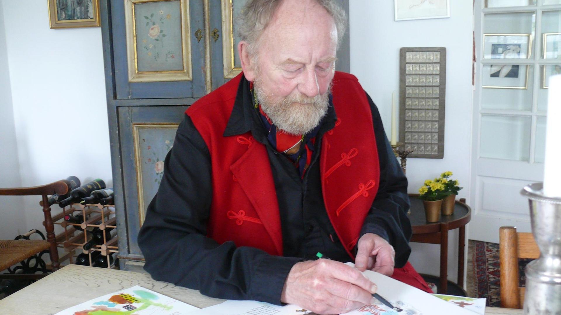 Der Karikaturist Kurt Westergaard sitzt an seinem Wohnzimmer am Tisch und zeichnet.