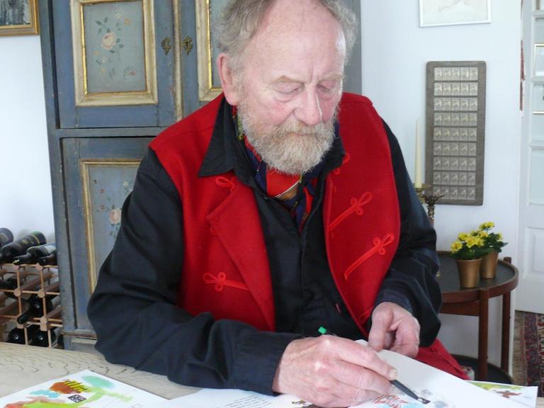 Der Karikaturist Kurt Westergaard sitzt an seinem Wohnzimmer am Tisch und zeichnet.